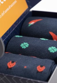 Drei Paar marineblaue Socken in einer Box, mit Mustern von roten Chilischoten, Kleeblättern und Herzen in gestrickter Textur.
