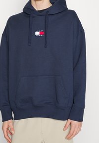 Felpa con cappuccio blu navy in cotone, dotata di una tasca frontale a marsupio e di una piccola etichetta con il marchio sul petto.