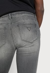 Grijze denim jeans met een slim fit, voorzien van twee achterzakken en een driehoekig merklogo op de rechterzak. Soepele textuur.
