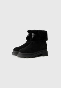 Bottines en suede noir avec un col en fausse fourrure noire et moelleux. Dotées d'une semelle noire robuste et d'un logo décoratif en forme de bouclier à l'avant.