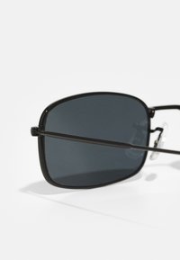 Schwarze Sonnenbrille mit rechteckiger Form, dunklen Gläsern, dünnem Metallrahmen und verstellbaren Nasenpads für einen optimalen Sitz. Minimalistisches Design mit klaren Linien.