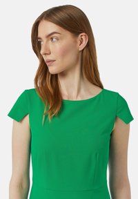 Grünes Kleid mit kurzen Ärmeln und rundem Ausschnitt. Glatter Stoff, taillierte Form und minimale Nahtdetails.