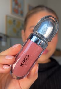 Brillo labial transparente en un envase transparente, con una tapa plateada. El producto es de un suave tono rosa con un ligero brillo. La etiqueta dice "KIKO MILANO."