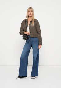Veste courte à carreaux marron, jeans évasés bleus, baskets noires et petit sac à bandoulière noir. Tissu lisse avec un design structuré.
