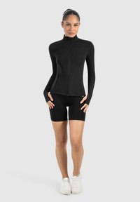 Black zip-up jacket with long sleeves and side pockets, paired with black shorts. Designed from stretchy material for a fitted look.