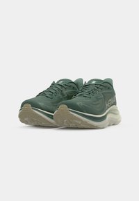 Grüne Sportschuhe mit einem strukturierten Mesh-Obermaterial, verstärkter Zehenpartie, gepolstertem Zwischensohlensystem und Gummisohle mit gerilltem Muster.