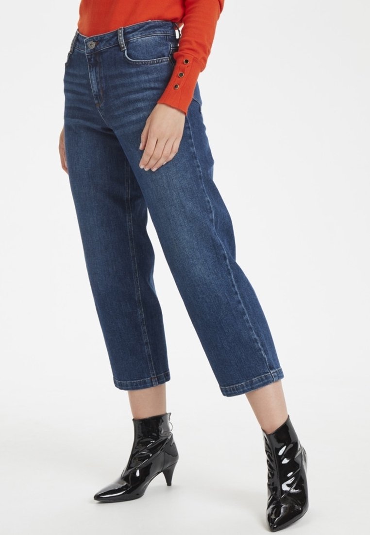 Jeans cortos de tiro alto en azul oscuro, con pierna recta y cinco bolsillos, combinados con botas negras hasta el tobillo y una blusa roja de manga larga.