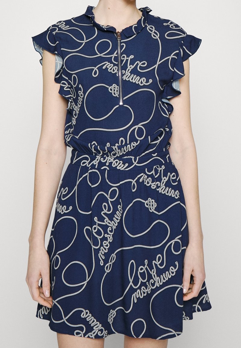 Marinblå klänning med volangärmar och dragkedja framtill. Har vit rep-stil "love" tryck, insnörd midja och utställd kjol.