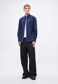 Siniste triipudega nööpidega särk kraega, ühendatud lahtiste tumedate teksade ja mustade kingadega. Näha on lihtne valge aluspluus.