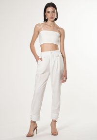 Witte cropped tanktop en hoge witte broek met knoopaccenten, met een rechte pijp en opgerolde manchetten. Soepele stofstructuur.