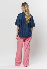 Džínová košeľa s krátkym rukávom v tmavomodrej farbe v kombinácii s širokými nohavicami s ružovými pruhmi. Texturovaná tkanina, voľný strih a zakrivený lem.