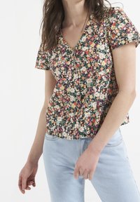 Blouse à manches courtes à fleurs en noir avec un mélange vibrant de fleurs roses, orange et blanches. Col en V avec fermeture à boutons et coupe ample.
