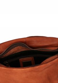 Interno di una borsa in pelle marrone che mostra una tasca con zip, una morbida fodera in suede e una texture liscia con una zip color oro.