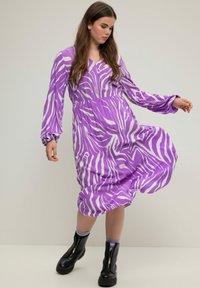 Fialové midi šaty s bílými pruhy zebra, dlouhými nafouknutými rukávy a véčkovým výstřihem; spárované s černými kotníkovými botami na zip. Hladká textura látky.