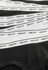 Mustat ja valkoiset alusvaatteet, joissa on "NEXT"-brändin logo elastisessa vyötärönauhassa. Musta kangas luo visuaalista vaikutusta valkoista vasten.