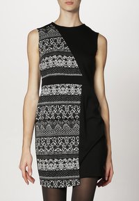 Robe noire sans manches avec un design asymétrique, une moitié en noir uni et l'autre ornée de motifs en noir et blanc complexes.