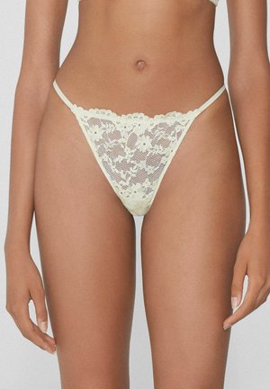 Lace string in lichtgeel, met bloemenpatronen, dunne zijbandjes en een golvende tailleband. Semi-transparante textuur.