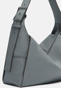 Szara skórzana torebka o trójkątnym kształcie, z regulowanym paskiem na ramię, minimalnym przeszyciem i gładką teksturą. Posiada zamek błyskawiczny.