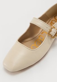 Pantofi bej din piele tip Mary Jane, cu vârf pătrat, având o curea îngustă și un detaliu din metal auriu pe catarama.