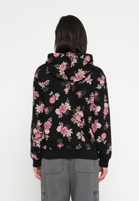 Czarna bluza z kapturem w kwiaty z różowymi i kremowymi różami, z kapturem ze sznurkiem oraz ściągaczami na mankietach i dole. Miękka tkanina o casualowym kroju.