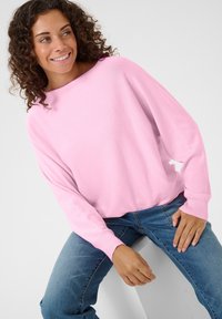 Roze, oversized trui met lange mouwen en geribbelde manchetten, gecombineerd met blauwe jeans. Zachte gebreide textuur, relaxte pasvorm.