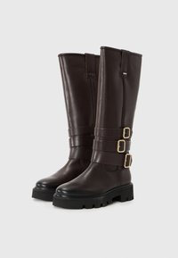 Bocanci din piele maro, până la genunchi, cu trei accente de cataramă, talpă texturată și design cu vârf rotunjit. Finisaj neted cu o siluetă elegantă.