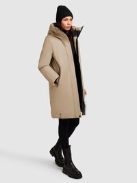 Beige isoleret parka med hætte, sidelommer og sort indvendig for. Kombineret med sorte leggings og chunky sorte ankelstøvler.