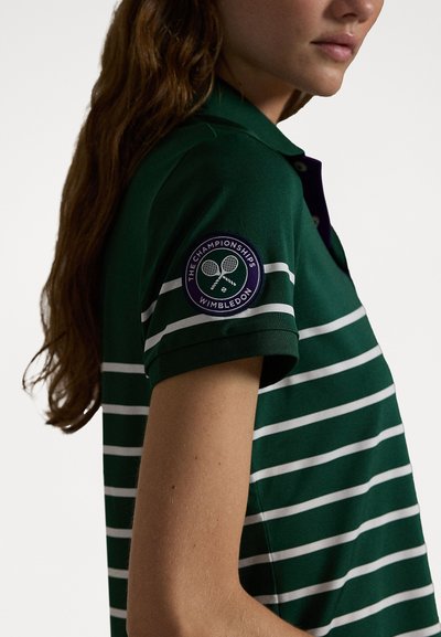 Grønn polo skjorte med hvite horisontale striper. Har en lilla sirkulær lapp med tennismotiver på venstre erme. Tradisjonell kragedesign.