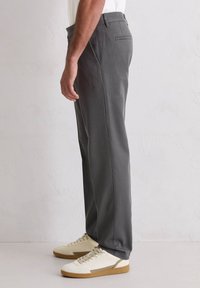 Graue Hose mit maßgeschneiderter Passform, seitlichen Taschen und glatter Textur. Kombiniert mit beigen Sneakern für einen lässigen Look.