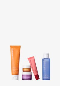 Four skincare products: orange cleanser tube, pink lip treatment, purple moisturizer, and blue toner bottle, showcasing vibrant colors and distinct shapes.