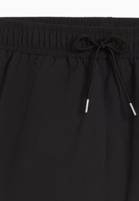 Pantaloni corti neri con vita elastica, dotati di chiusura con cordino e estremità in metallo argentato. Tessuto morbido, leggero e confortevole.