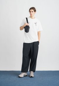 Vit bomullströja med grafik, svarta lösa byxor och grå sneakers. Liten svart axelremsväska med dragkedja.