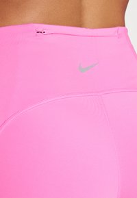 Kadar izbliza osobe koja nosi svijetlo ružičaste Nike sportske kratke hlače s vidljivim šavovima i malim srebrnim Nike swoosh logotipom.