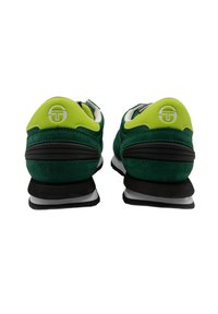 Baskets de sport vertes et noires avec une texture en cuir suédé, talon arrondi et logo bien visible au niveau du talon. Elles disposent d'un col rembourré et d'accents contrastants.