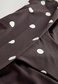 Brown fabric with white polka dots, smooth texture, folded to display pattern and color contrast. Material appears stretchy and soft.