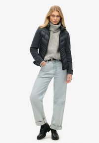 Chaqueta de plumas negra sobre un cuello de tortuga de punto gris, pantalones vaqueros de tiro alto en azul claro y botas negras con cordones. Corte relajado con puños doblados.