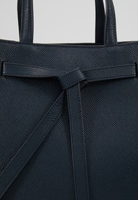 Borsa in pelle blu scuro con texture, caratterizzata da un dettaglio a nodo sul davanti, con due manici robusti e una finitura liscia.