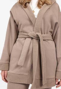 Roba beige con un collo e polsini in pile morbido e testurizzato. Presenta una cintura abbinata legata in vita, con una vestibilità ampia e rilassata.