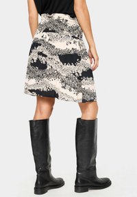 Jupe imprimée noir et crème avec un design évasé et un motif floral, assortie à des bottes en cuir noires montant jusqu'aux genoux. Taille cintrée avec une finition texturée.