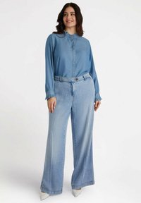 Camisa de mezclilla azul clara con botones en el frente y puños acampanados, combinada con jeans de pierna ancha en azul claro. Tejido texturizado, ajuste relajado.