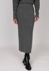 Jupe longue en tricot côtelé grise avec une taille ajustée, présentant une silhouette droite, associée à des bottines noires et des chaussettes côtelées.