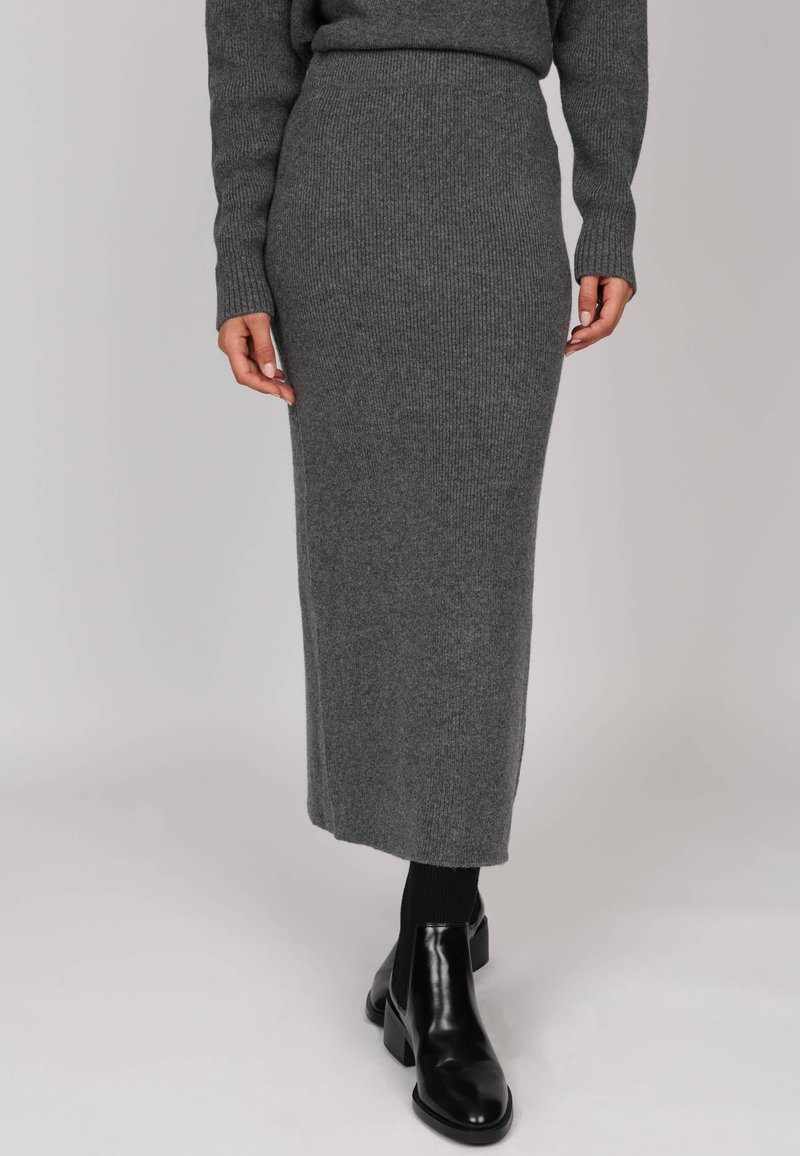 Jupe longue en tricot côtelé grise avec une taille ajustée, présentant une silhouette droite, associée à des bottines noires et des chaussettes côtelées.