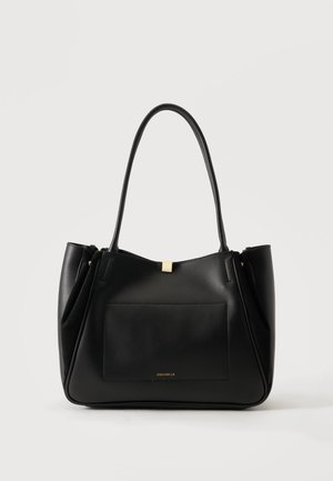 Sac fourre-tout en cuir noir avec longues poignées, poche avant et petit logo de marque doré sur fond neutre.