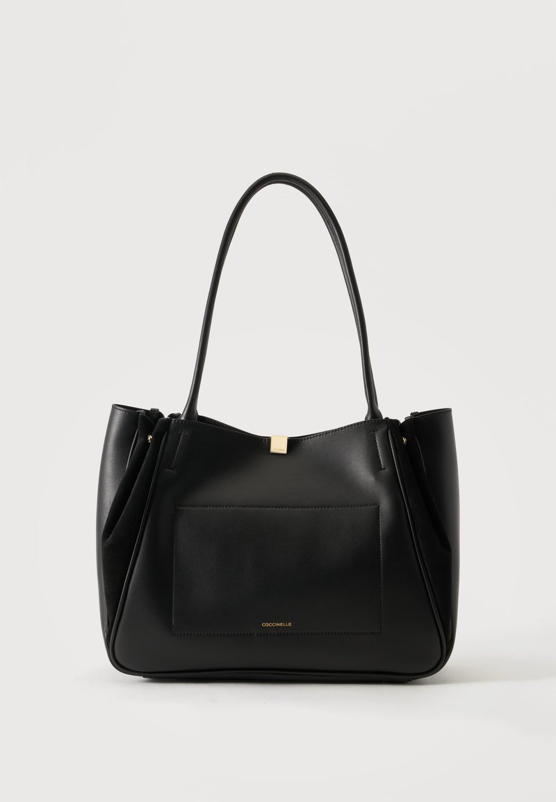 Sac fourre-tout en cuir noir avec longues poignées, poche avant et petit logo de marque doré sur fond neutre.