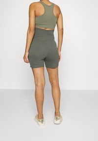 Olivově zelený sportovní crop top a šortky s vysokým pasem, hladká textura, přiléhavý střih, zobrazený pohled zezadu, spojený s béžovými teniskami.