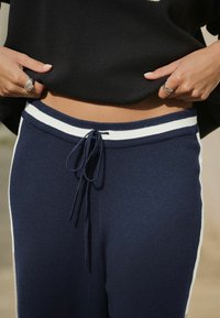 Navy jogger pants with a white striped waistband, drawstring closure, and textured fabric. Paired with a black top.