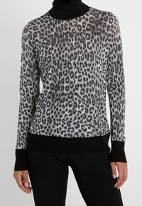 Długi top z długim rękawem w cętki lamparta w kolorach czarnym i szarym, z golfem oraz czarnym prążkowanym wykończeniem na dole i mankietach. Półprzezroczysta tkanina.