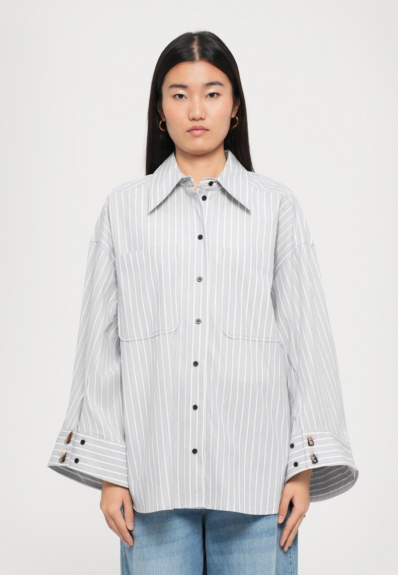 Striped button-up shirt in light gray and white, features a classic collar, two chest pockets, and wide bell sleeves with button details.