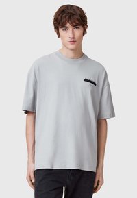 Camiseta de algodón gris claro con manga corta, corte relajado, escote redondo y un pequeño detalle de logo negro en el pecho.