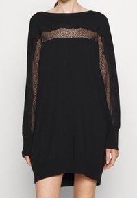 Robe noire oversize avec des panneaux en dentelle sur la poitrine et les manches, présentant une coupe ample et des manches longues. Matière en maille douce.